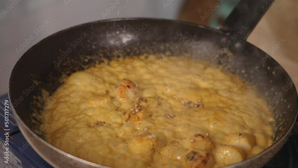 Chef grinding some salt, seasoning and adding more flavour into simmering creamy coconut curry seafood scallops in shallow frying pan, dinner preparation close up shot. Chef grinding some salt, seasoning and adding more flavour into simmering creamy coconut curry seafood scallops in shallow frying pan, dinner preparation close up shot.