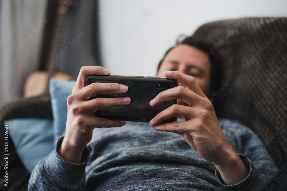 Young, handsome man playing on his smartphone at home on a couch Young, handsome man playing on his smartphone at home on a couch