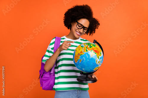 Portrait of attractive cheerful girl learner holding globe find continent mainland isolated on bright orange color background