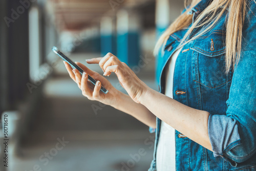 Photo of Young business woman wearing casual clothing calling mobile phone while standing with blurred car in parking lot. Side view of Beautiful, happy Caucasian female using smartphone device