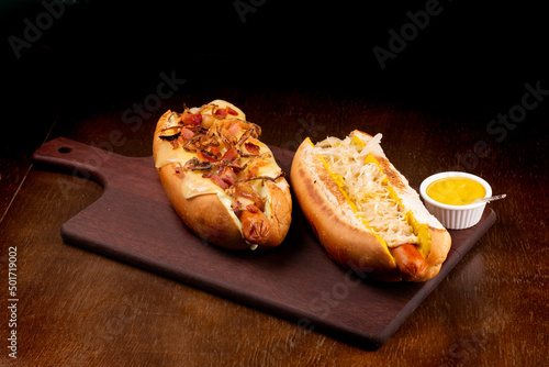 two american hot dogs with crispy bacon cheese and onions and german with mustard sauerkraut on board angle view