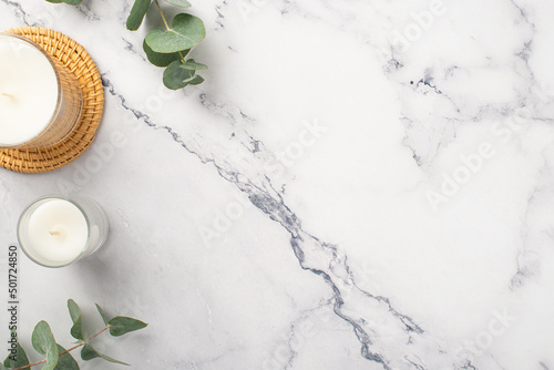 Top view photo of candles on rattan serving mat and eucalyptus on white marble background with copyspace © ActionGP