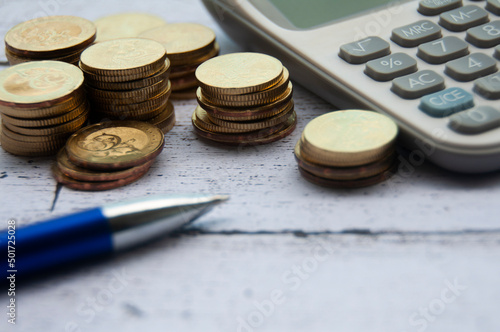 Gold coins, calculator and pen on wooden background. Selective focus on gold coins.