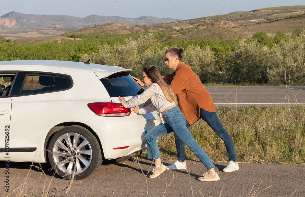 Man and woman pushing a white broken car, back view. In the middle of nowhere in the countryside Man and woman pushing a white broken car, back view. In the middle of nowhere in the countryside