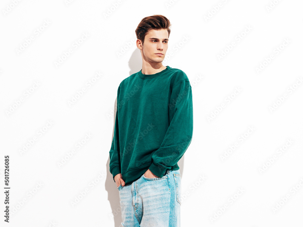 Fototapeta premium Portrait of handsome confident stylish hipster lambersexual model.Man dressed in green sweater and jeans. Fashion male posing in studio near white wall. Isolated