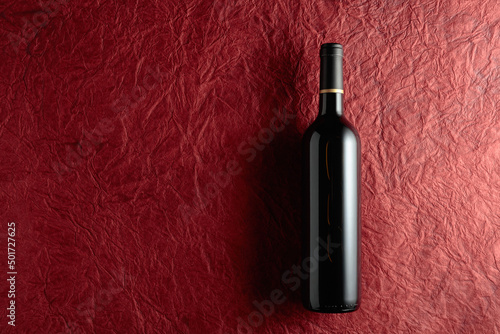 Bottle of red wine on a crumpled red paper background.