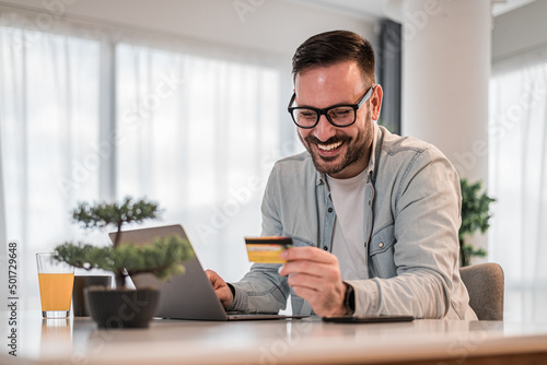 Smiling businessman making online payment with credit card from laptop at desk