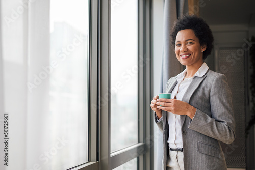 Portrait of confident smiling business woman enjoying coffee by window at office Free Download Portrait of confident smiling business woman enjoying coffee by window at office - GFXLoad
