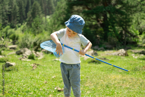 Little boy is walking with butterfly net and catching butterflies on green hills on sunny summer day