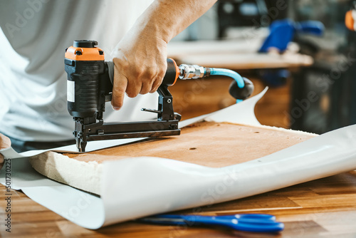 carpenter using  nail gun or staple gun after replace a vinyl or  upholstery fabric to the Seat for Bar Stools,furniture restoration woodworking concept. selective focus photo