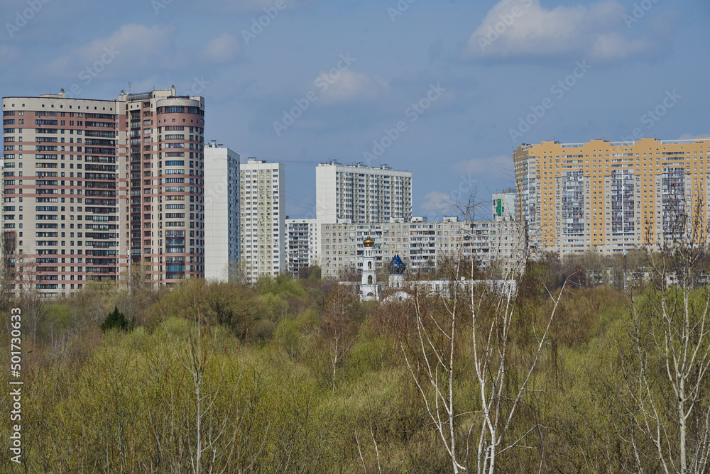 An urban residential area rises above a green park against a blue sky.