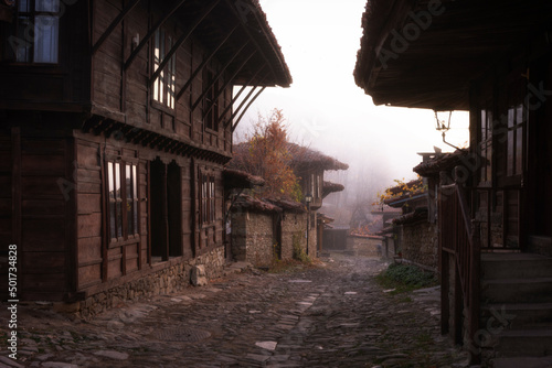 Wallpaper Mural Foggy autumn morning at a street of small village Zheravna in Bulgaria. Traditional historical wooden houses and first light of sun reflecting in the windows. Tourism, travel concept. Torontodigital.ca