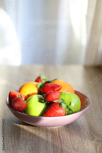 Fototapeta Naklejka Na Ścianę i Meble -  Pink bowl filled with fresh apples, oranges and strawberries on wooden table. Selective focus.