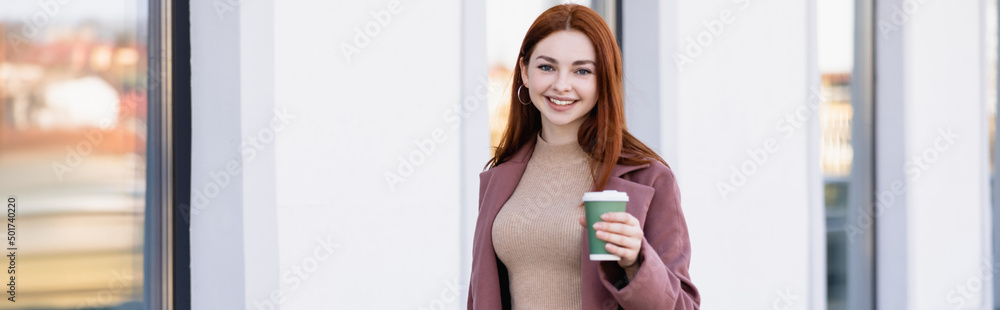 cheerful woman holding coffee to go on urban street, banner. cheerful woman holding coffee to go on urban street, banner.