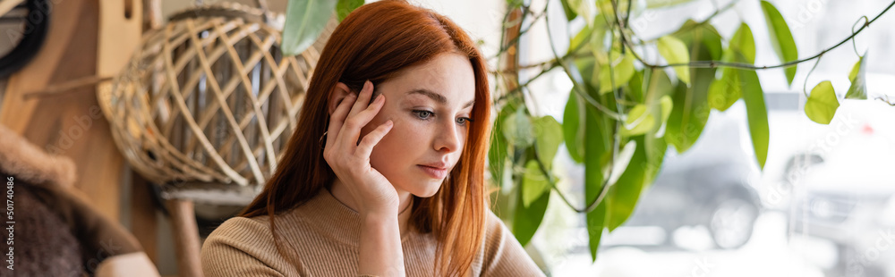 young redhead woman holding hand near cheek in cafe, banner. young redhead woman holding hand near cheek in cafe, banner.