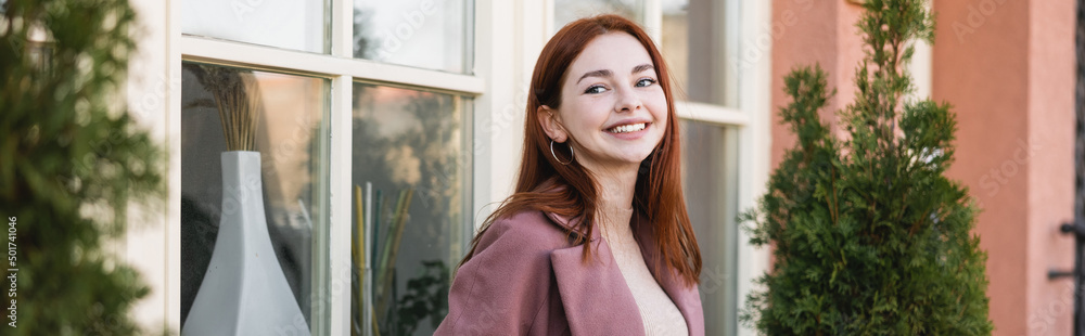 young cheerful woman with red hair standing near building, banner. young cheerful woman with red hair standing near building, banner.