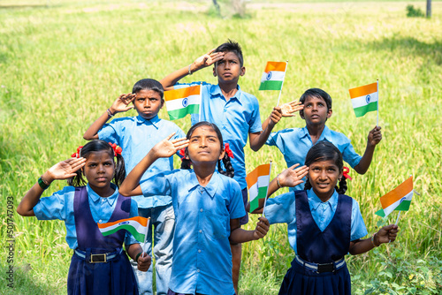 Obraz na płótnie Group of village school children with Indian flag in hand saluting by looking ab