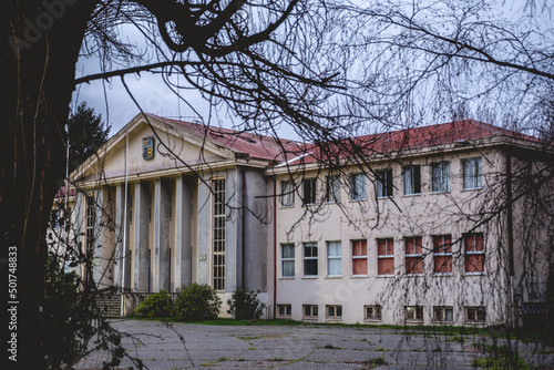 Beautiful old centuries building (now used as public university) with neoclassical style, columns and triangle roof in facade, trees, branches, grass and cloudy sky, Valdivia, Chile photo