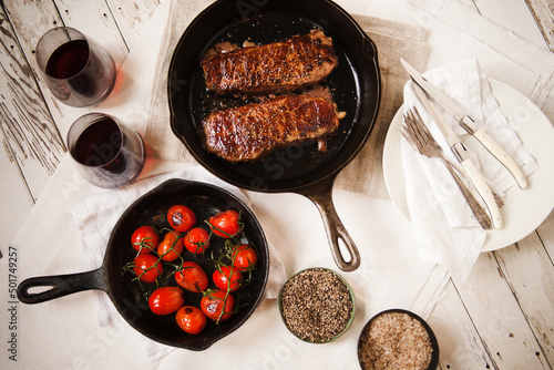 Cast iron pans with strip steaks and tomatoes with red wine photo