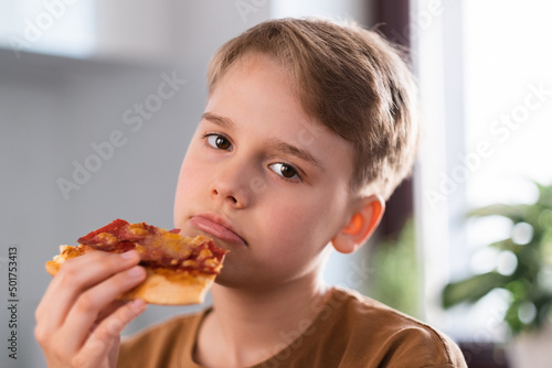 Sad teen boy enjoying eating delicious pizza at home.