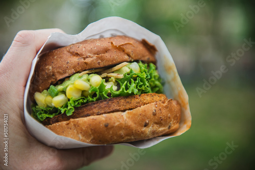 A hand holding a veggie burger with corn, lettuce and guacamole. photo