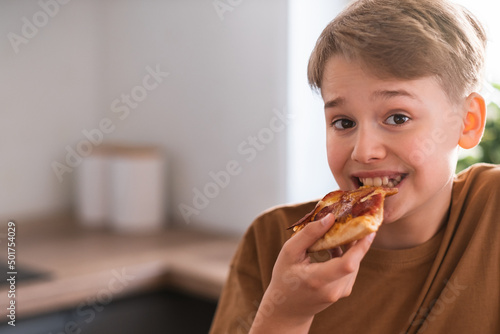 Happy teenager enjoying eating delicious pizza at home. Freshly baked pepperoni pizza