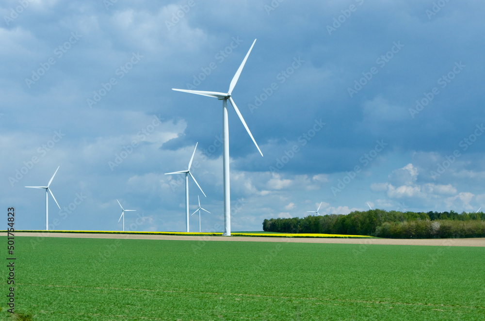 Rural landscape in France with blue sky and green field with spinning wind power stations producing environmentally friendly electric energy. Rural landscape in France with blue sky and green field with spinning wind power stations producing environmentally friendly electric energy.