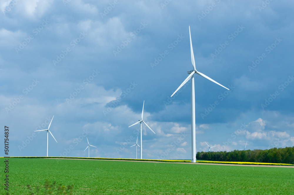 Rural landscape in France with blue sky and green field with spinning wind power stations producing environmentally friendly electric energy. Rural landscape in France with blue sky and green field with spinning wind power stations producing environmentally friendly electric energy.