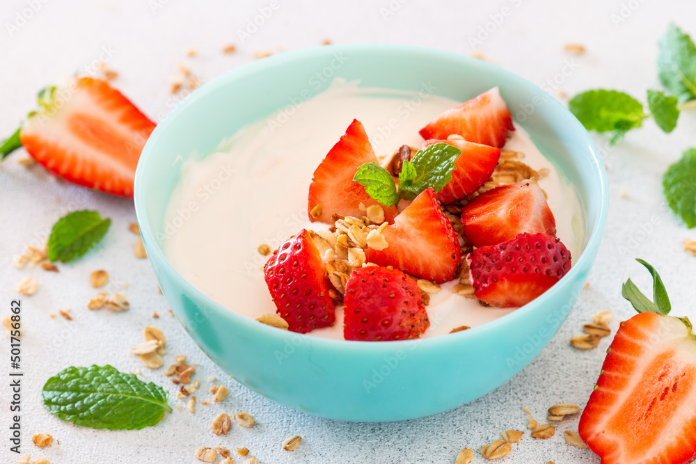 Yogurt with granola and strawberry in blue bowl at light stone table. Close up. Yogurt with granola and strawberry in blue bowl at light stone table. Close up.