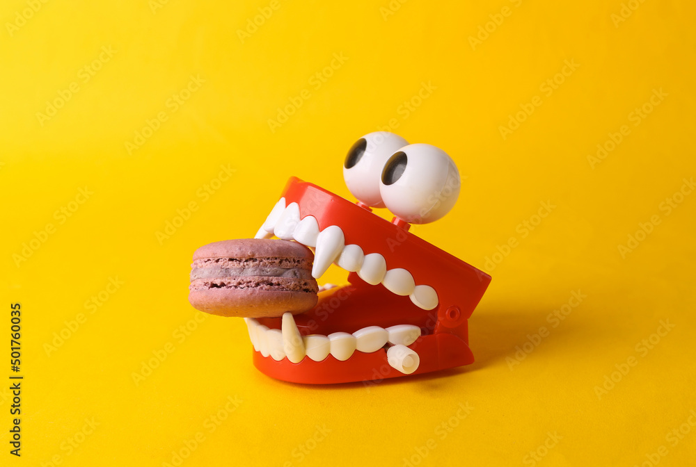 Toy jaw vampire with french macaroon in the teeth on yellow background. Halloween concept