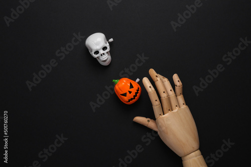 Wooden hand with skeleton head and jack pumpkin on black background. Minimal halloween layout. Top view. flat lay photo