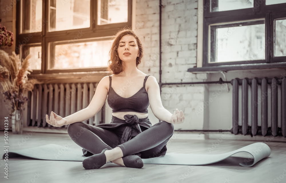 Young brunette woman in sportswear sits on the mat and meditates in the yoga studio Young brunette woman in sportswear sits on the mat and meditates in the yoga studio
