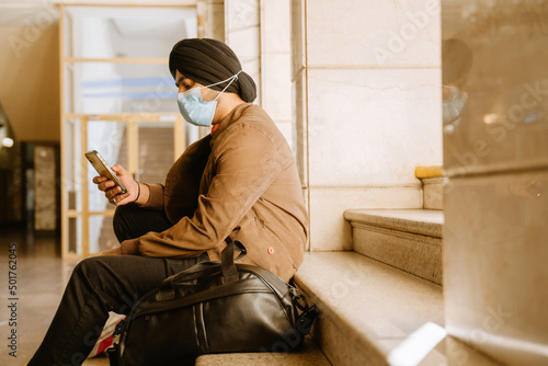 Indian man wearing face mask using mobile phone while sitting on stairs