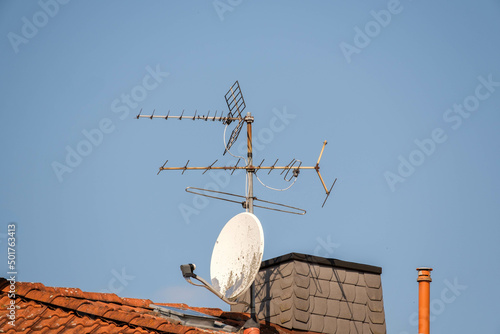 Satellite dish and old TV antenna on a red roof