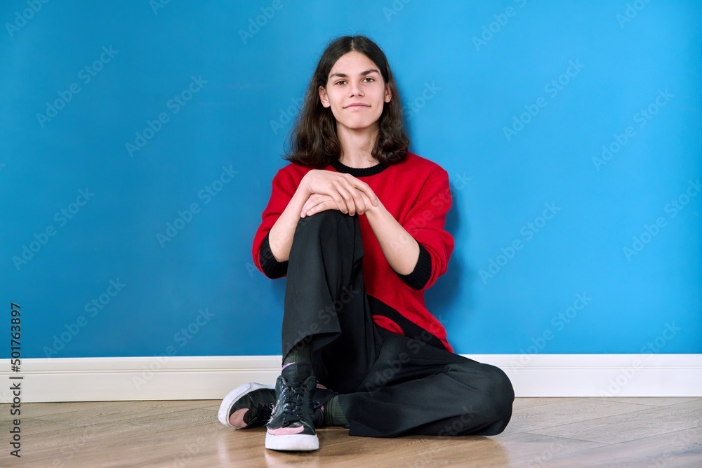 Portrait of young teenage guy sitting on the floor on blue background