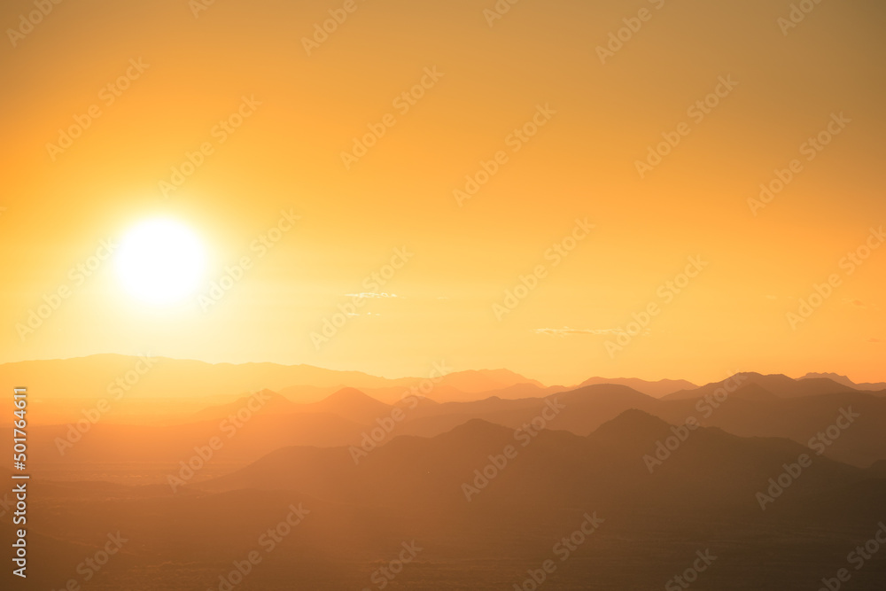 The sun setting behind the mountains of the Sonoran Desert in Arizona with the air lit up in golden light with mountains in silhouette. The sun setting behind the mountains of the Sonoran Desert in Arizona with the air lit up in golden light with mountains in silhouette.