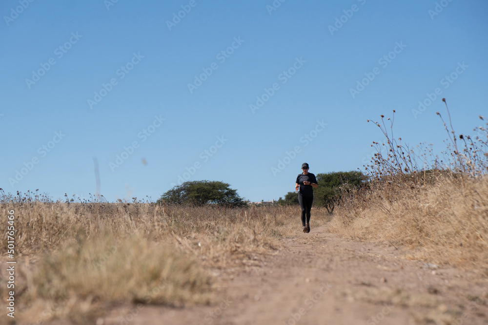 Woman wearing black runs on a trail at a field near Mineral del Pozos Woman wearing black runs on a trail at a field near Mineral del Pozos