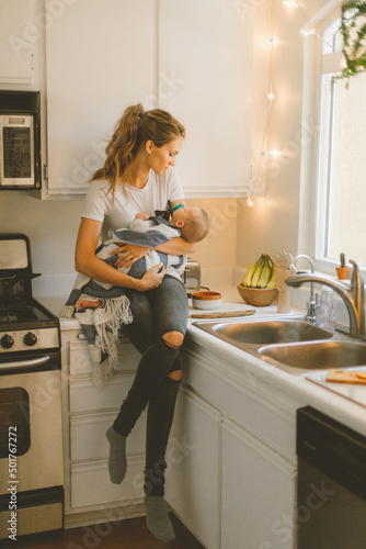 Mother holding infant while sitting on the counter in small kitc photo