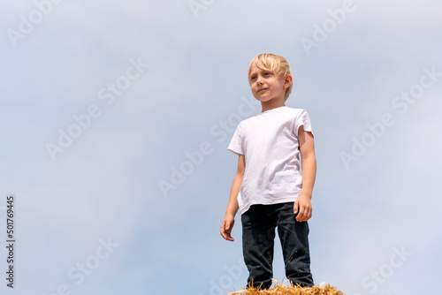 Fair-haired boy teenager in white T-shirt on blue sky background. Summer vacation. Bottom view photo