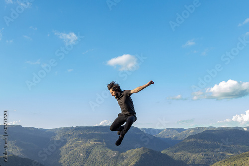 Young man dressed in black clothes jumping on mountains and blue sky background, in Nova Petropolis, Rio Grande do Sul sierra, Brazil