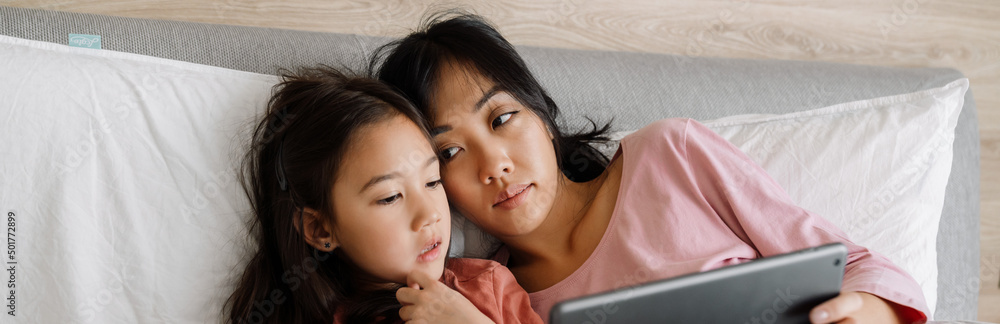 Asian mother and daughter using laptop while sitting on bed Asian mother and daughter using laptop while sitting on bed