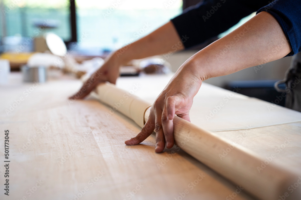 Close up of female hands working with rolling-pin for italian fresh pasta -  Female hands rolling  for fresh dough on the wooden table - concept of cooking and fresh homemade pasta