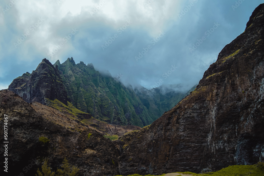 The gorgeous rugged wilderness and cliffs of Kauai's Napali Coast in Hawaii, with low clouds and mist hanging over the mountain peaks under a stormy grey sky