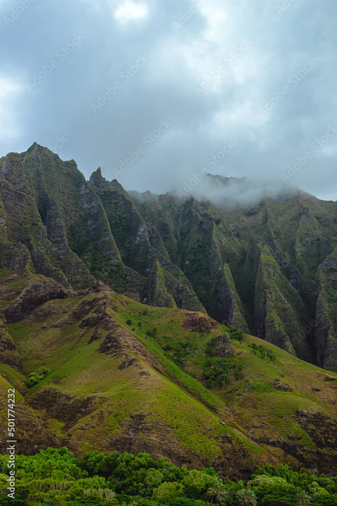 The gorgeous rugged wilderness and cliffs of Kauai's Napali Coast in Hawaii, with low clouds and mist hanging over the mountain peaks under a stormy grey sky