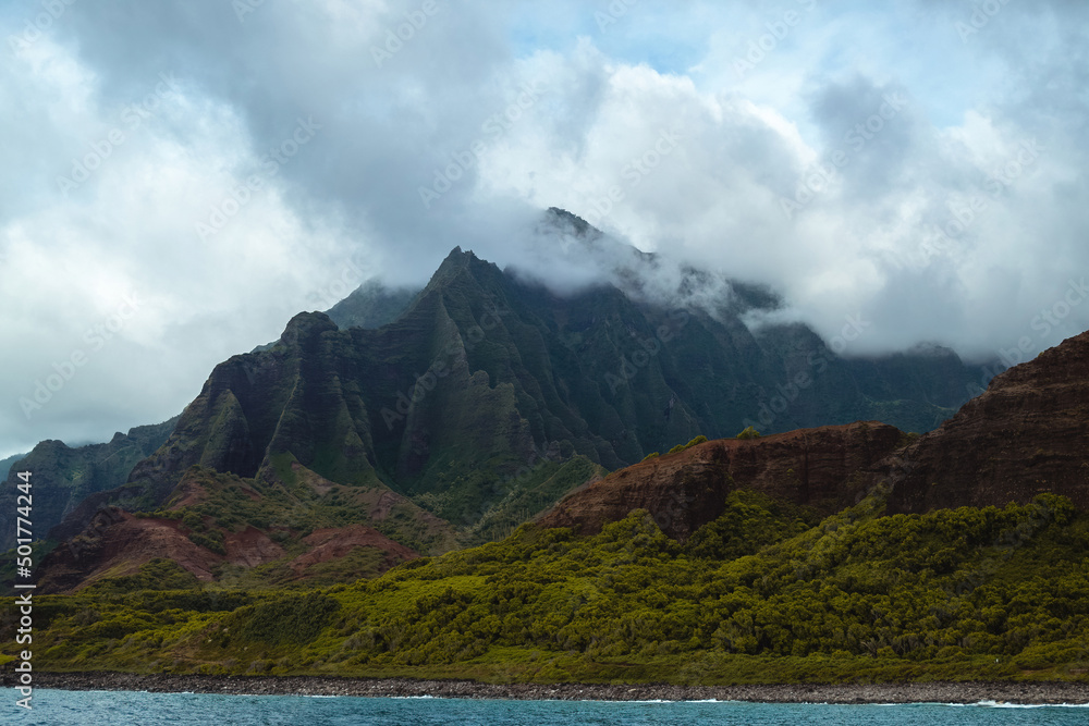 The gorgeous rugged wilderness and cliffs of Kauai's Napali Coast in Hawaii, with low clouds and mist hanging over the mountain peaks under a stormy grey sky The gorgeous rugged wilderness and cliffs of Kauai's Napali Coast in Hawaii, with low clouds and mist hanging over the mountain peaks under a stormy grey sky