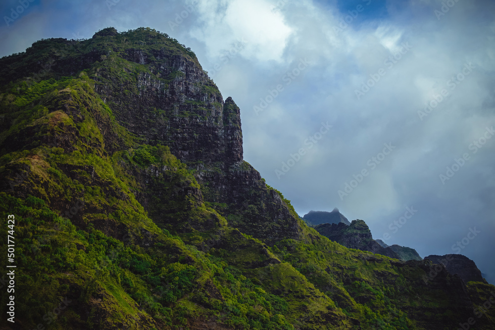 The gorgeous rugged wilderness and cliffs of Kauai's Napali Coast in Hawaii, with low clouds and mist hanging over the mountain peaks under a stormy grey sky