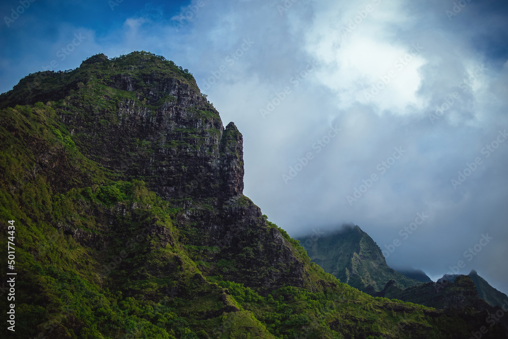 The gorgeous rugged wilderness and cliffs of Kauai's Napali Coast in Hawaii, with low clouds and mist hanging over the mountain peaks under a stormy grey sky The gorgeous rugged wilderness and cliffs of Kauai's Napali Coast in Hawaii, with low clouds and mist hanging over the mountain peaks under a stormy grey sky