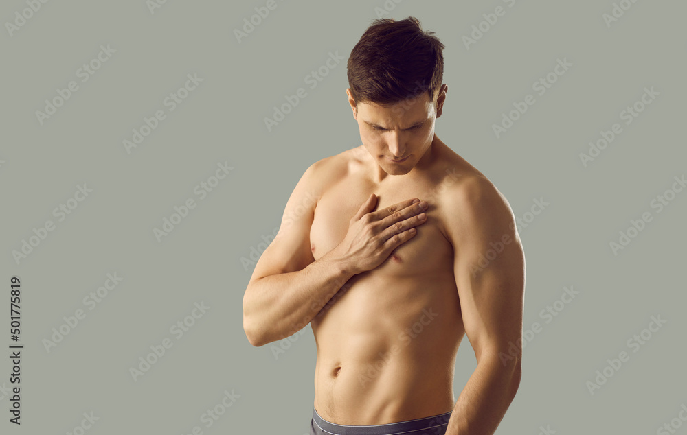 Fototapeta premium Naked sexy young man model in underwear isolated on grey studio background suffer from heart attack or disease. Toned muscular guy have pain in chest struggle with cardiovascular illness.
