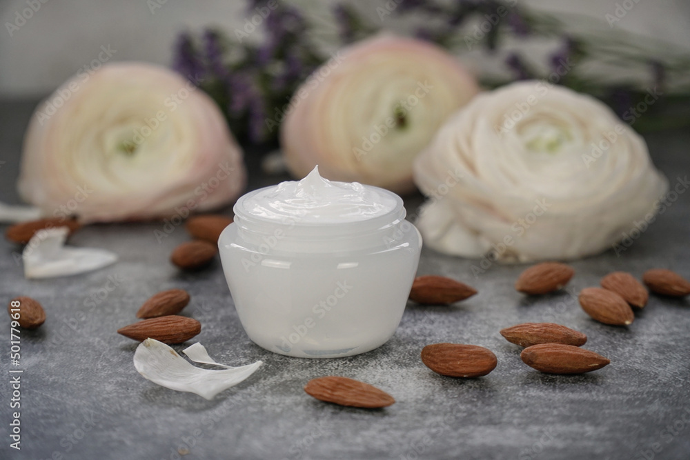  Face or body cream with almonds on grey background with real flowers. 