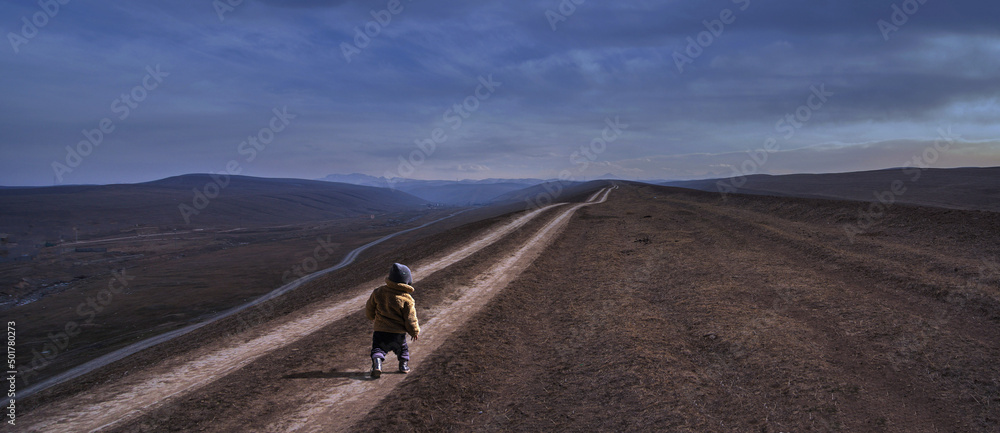 A lonely little child on a trampled road in the mountains.
